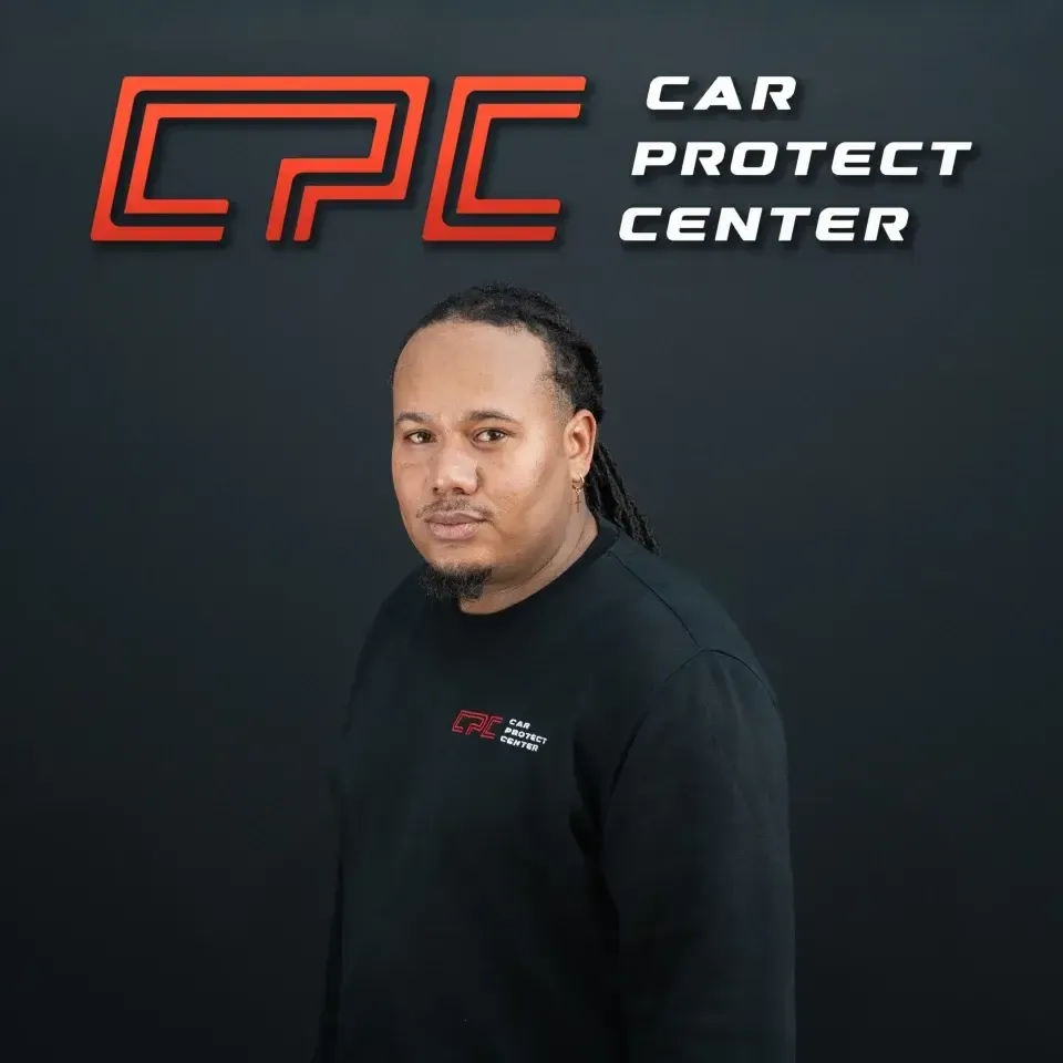 Portrait de studio d’un membre de l’équipe Car Protect Center, de trois quarts, devant le mur au logo CPC