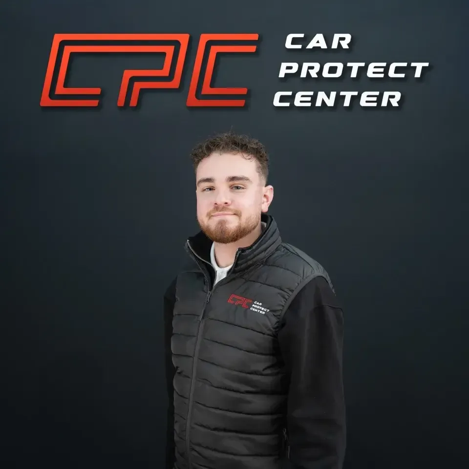 Portrait de studio d’un membre de l’équipe Car Protect Center, de trois quarts, devant le mur au logo CPC