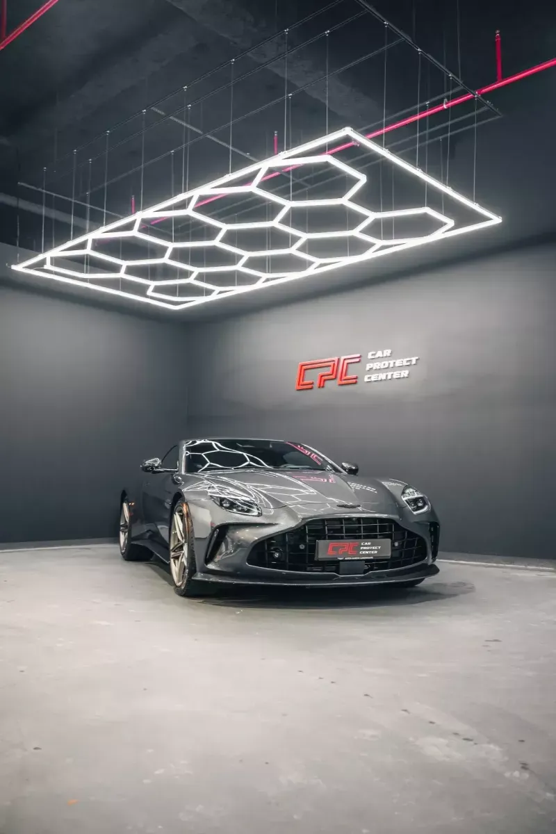 Coupé de sport gris anthracite seul dans l’atelier, sous l’éclairage hexagonal et le logo CPC