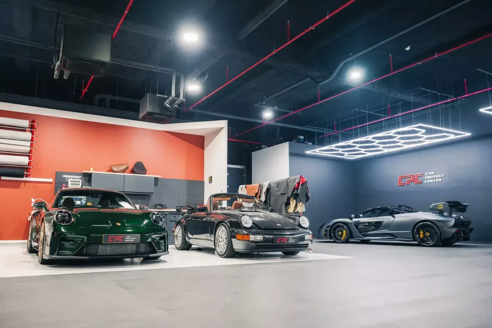 L’espace sellerie au mur orange, ses rouleaux de film et une Porsche 911 GT3 verte aux jantes dorées