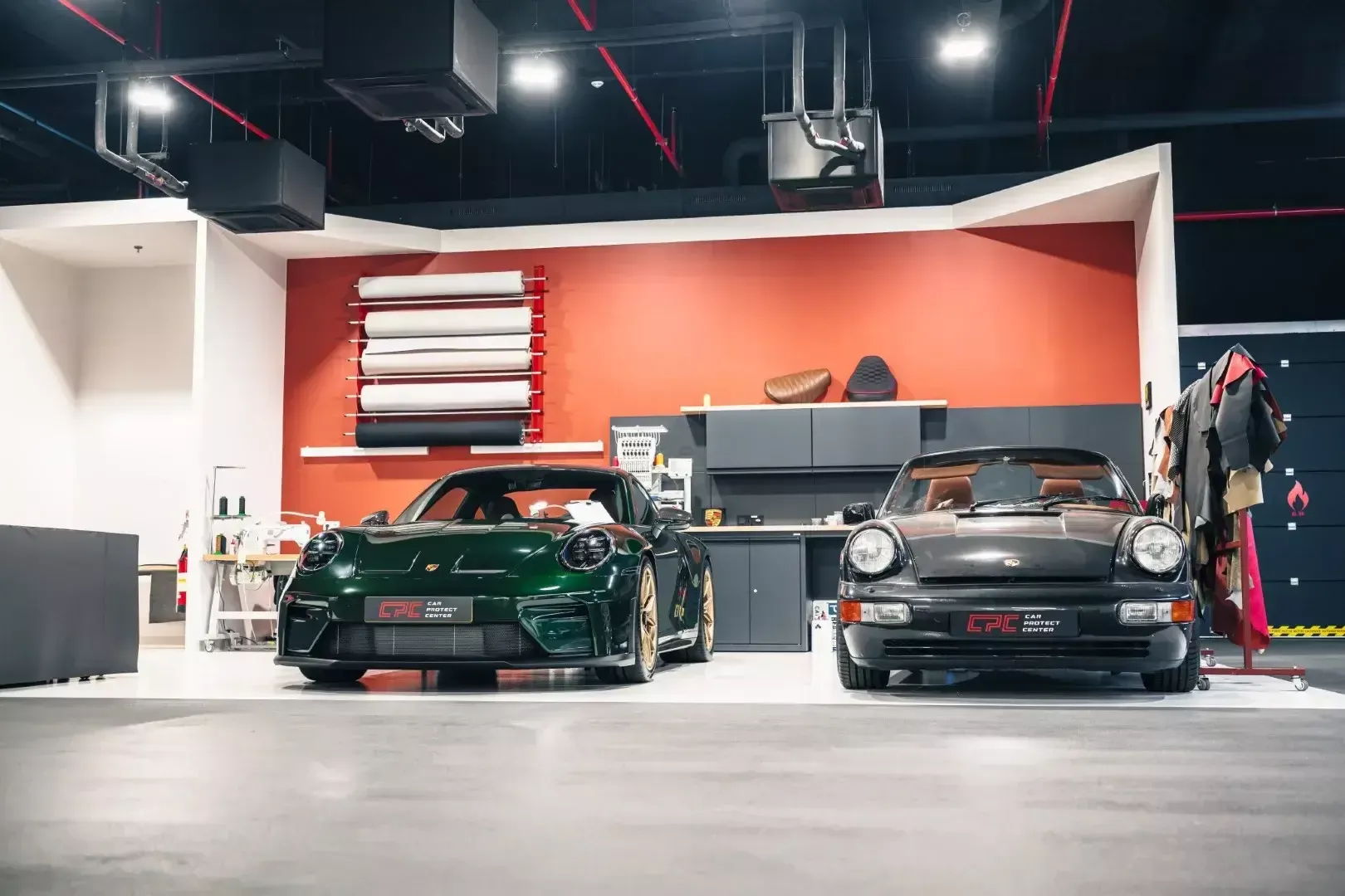 Deux Porsche devant l’atelier de sellerie : rouleaux de film, machines à coudre et cuirs sur portant
