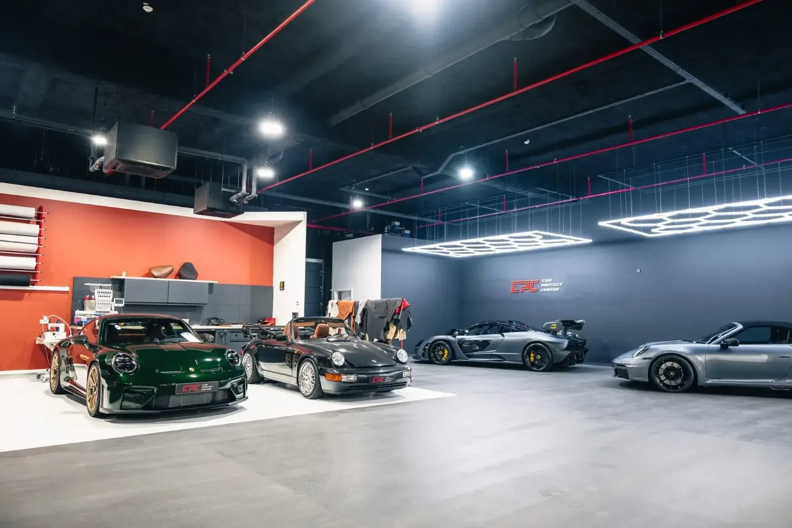Vue large de l’atelier : Porsche et McLaren alignées sous les luminaires hexagonaux du plafond