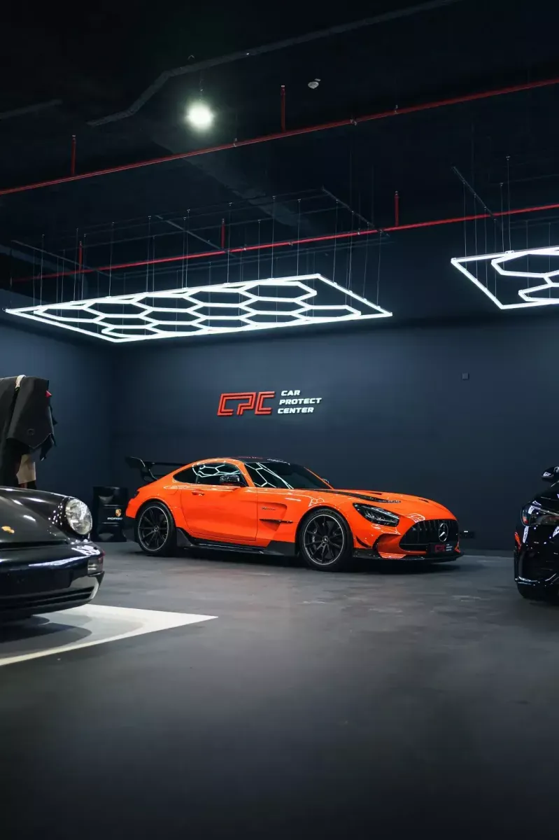 Mercedes-AMG GT orange de profil dans l’atelier, entre deux autres voitures de sport