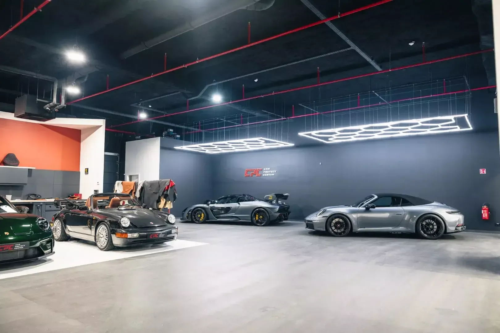 Vue d’ensemble de l’atelier, du mur orange de la sellerie jusqu’aux Porsche et à la McLaren