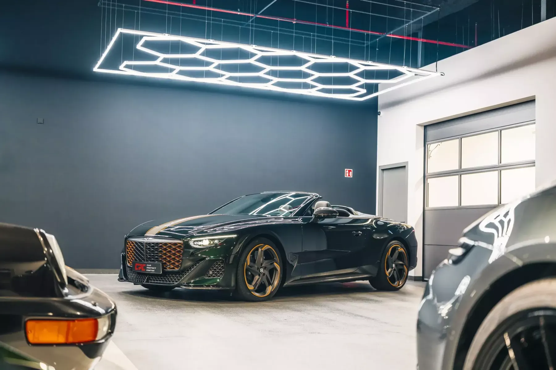 Cabriolet Bentley vert foncé aux jantes dorées, sous l’éclairage hexagonal de l’atelier