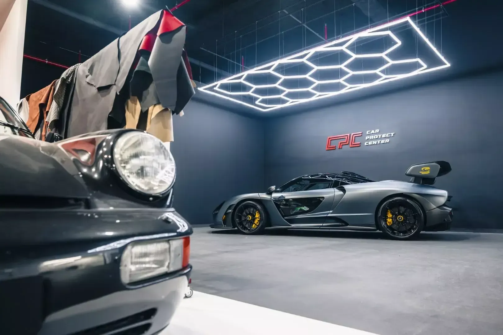 McLaren argentée dans l’atelier, à côté d’une Porsche classique et d’échantillons de cuir suspendus