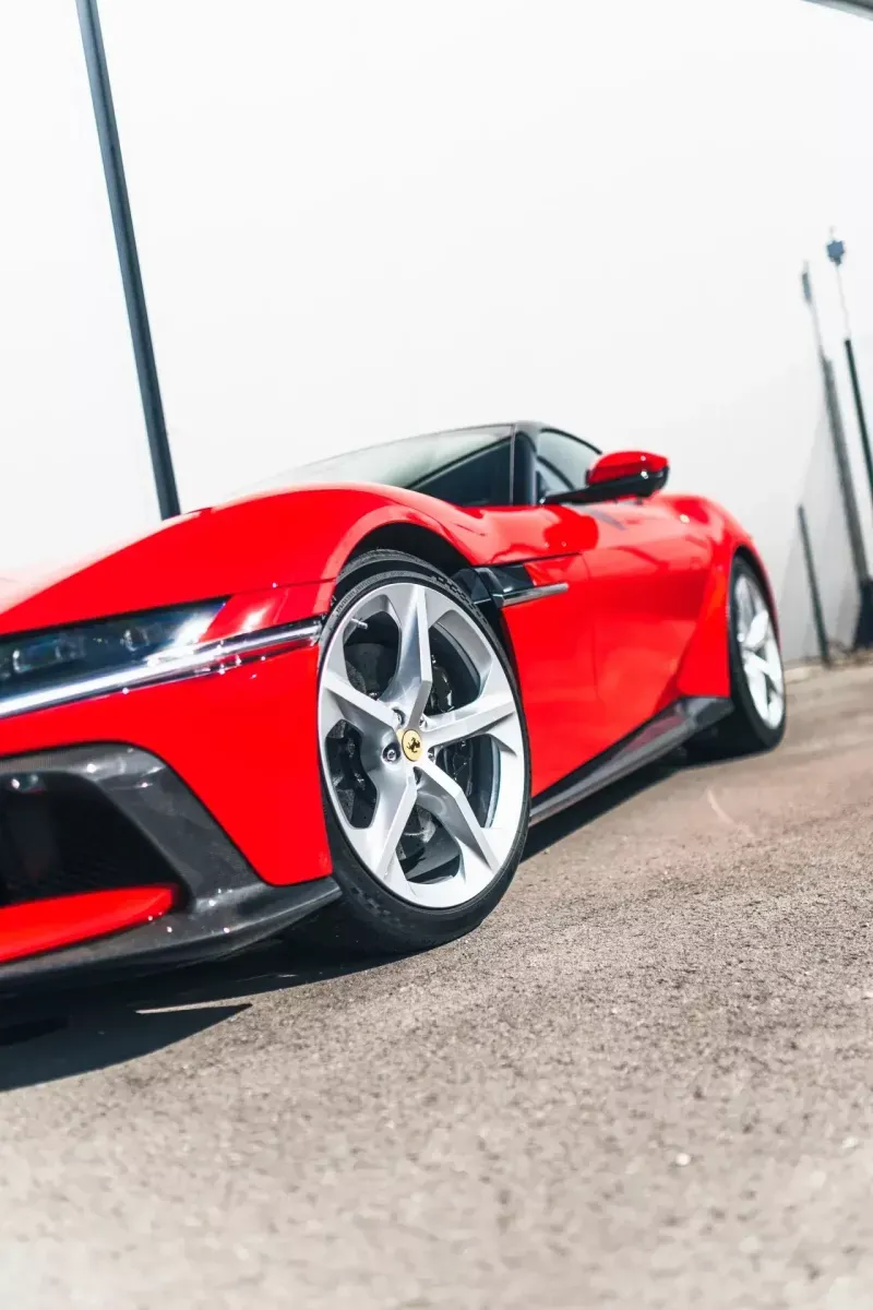 Gros plan sur l’avant et la jante d’une Ferrari rouge, devant l’atelier